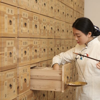 Woman looking through a drawer of Chinese medicine in a wall full of drawers